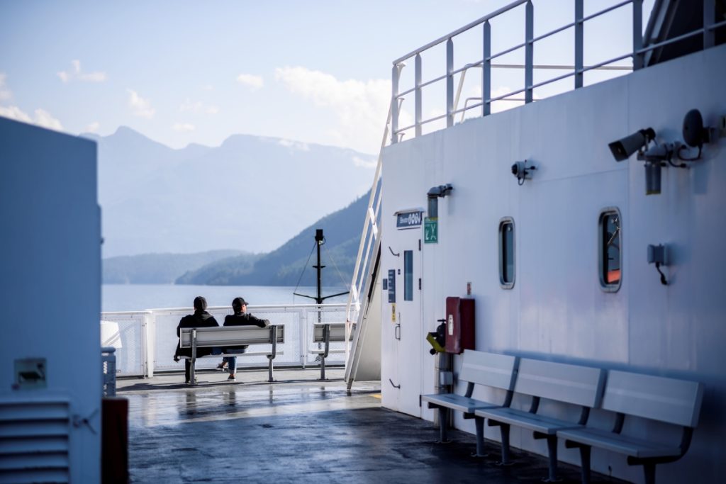 A couple sits on the deck of a ferry, taking in the view of the mountains.