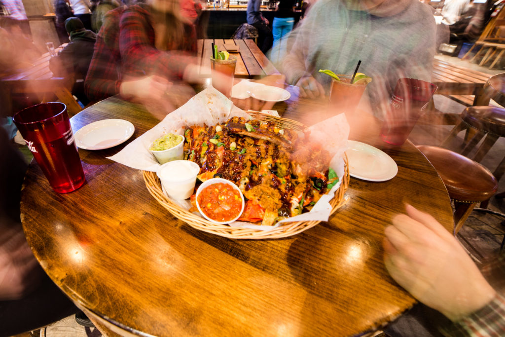 A group of diners enjoy a plate of pulled pork nachos.