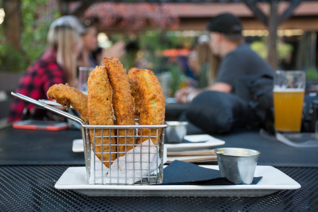 A basket of deep fried pickles sits on a table at an outdoor dining area.