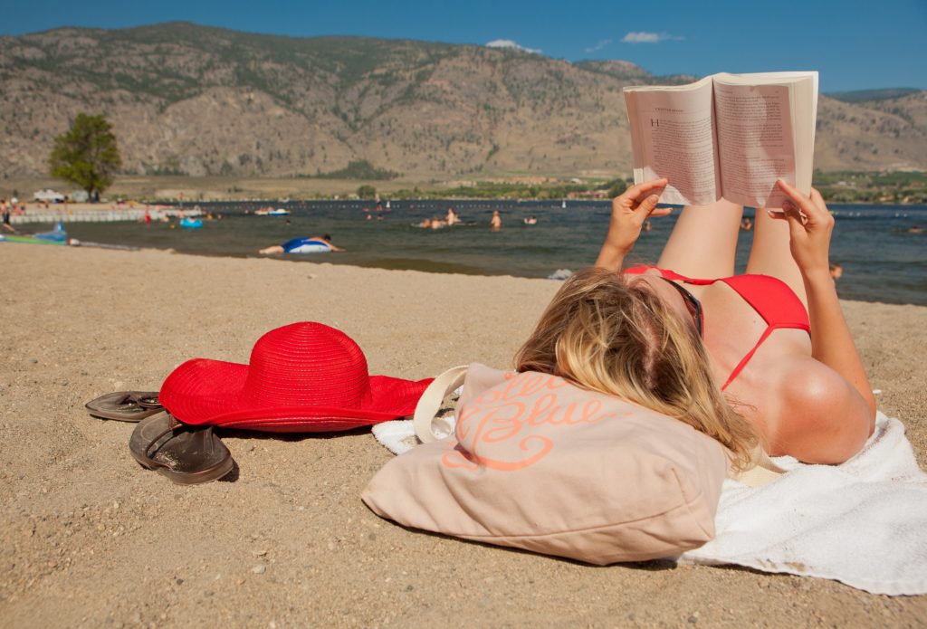 A woman in a red bathing suit reads a book on the beach.