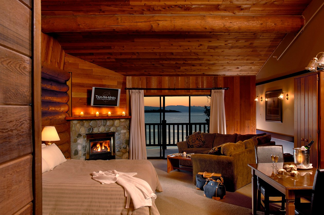 A luxurious hotel room with a fireplace and private balcony balcony overlooking the water at sunset.