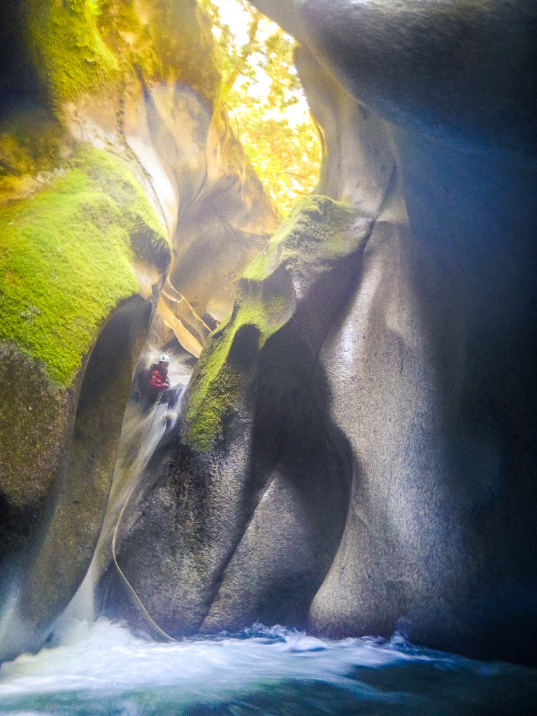 A woman rappels down a waterfall inside a canyon.