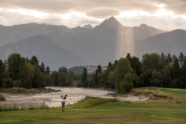 A golfer tees off on a lush golf course with mountain views.