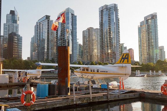 Two seaplanes are docked at a harbour as the Vancouver skyline rises in the background.