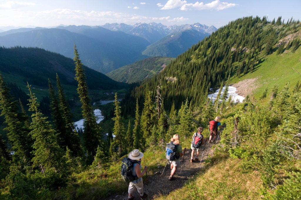 A group of hikers follow a path that overlooks a lush green valley.