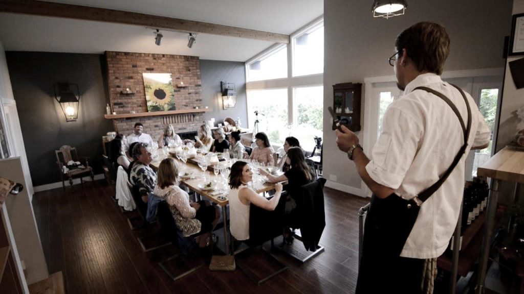A chef speaks to diners seated in a modern dining room.