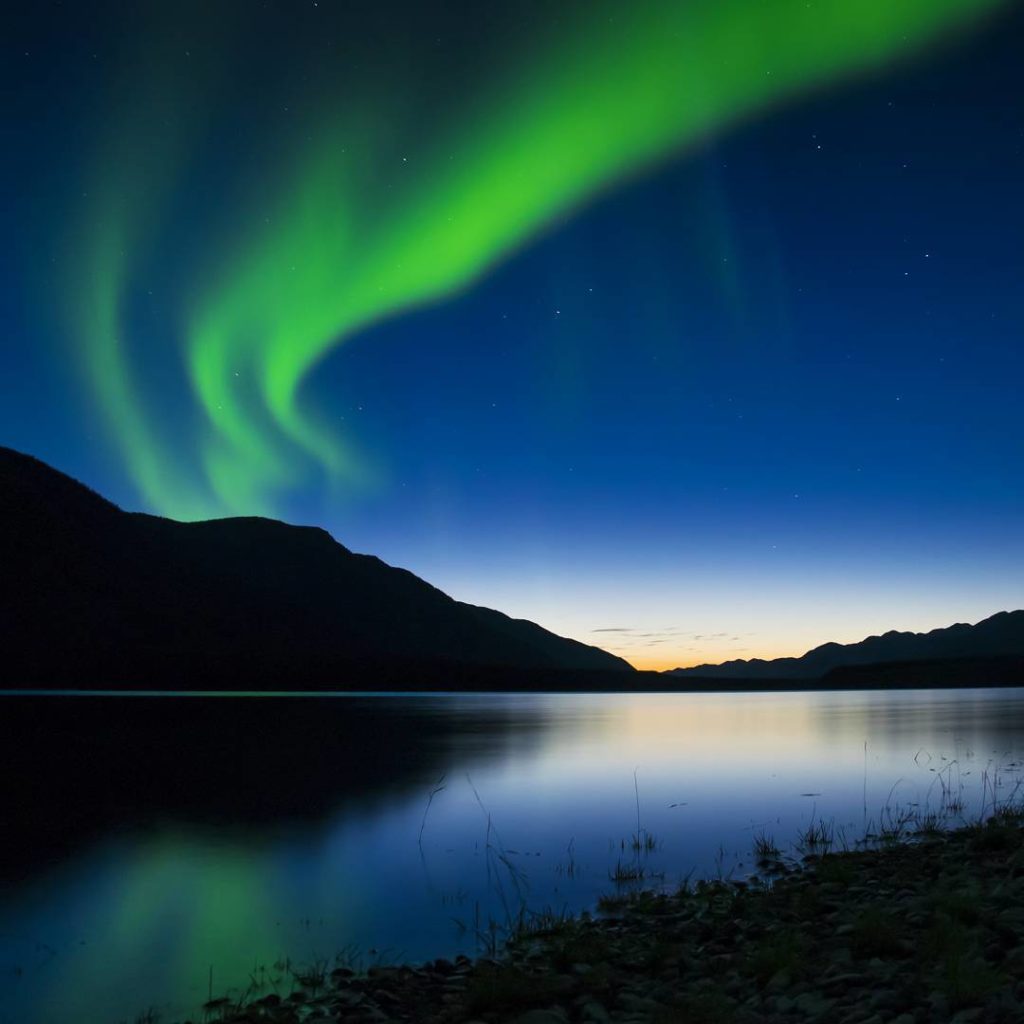 The Northern Lights shine neon green over a tranquil lake.