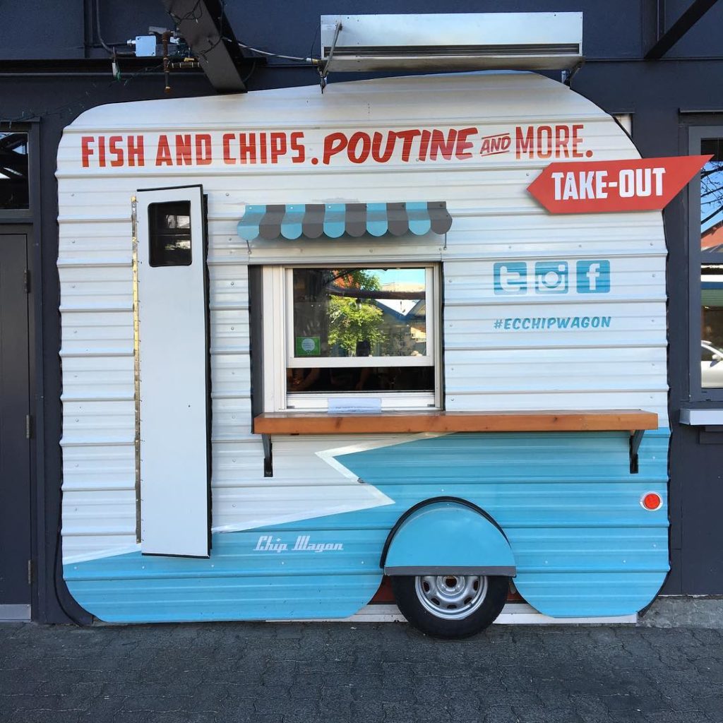 A small white and blue food truck with the words “Fish and Chips. Poutine and More!” on the side.