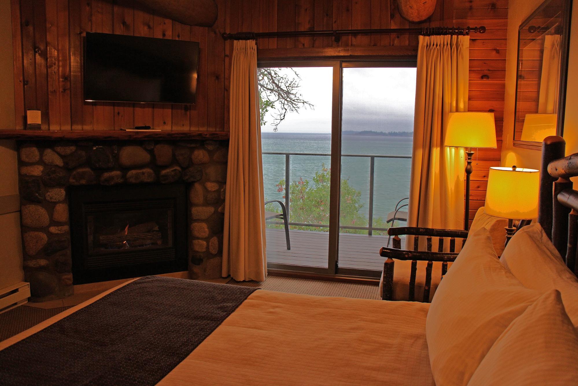 The cozy interior of a resort bedroom with a fireplace and private balcony overlooking the water.