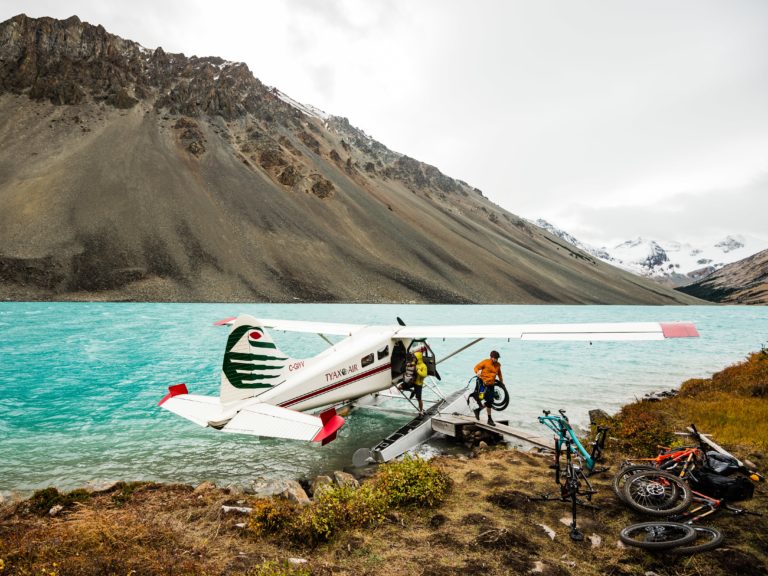 Mountain bikes are offloaded from a sea plane that has landed in turquoise waters.