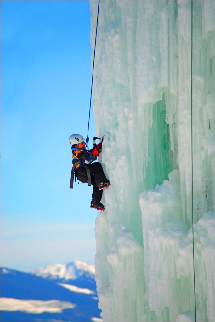 A young boy scales a thick wall of white ice.