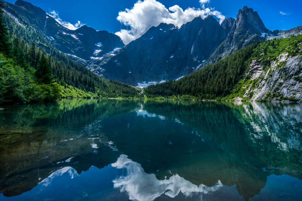 A sprawling mountain range and blue sky are reflected in still waters nestled in a lush valley.