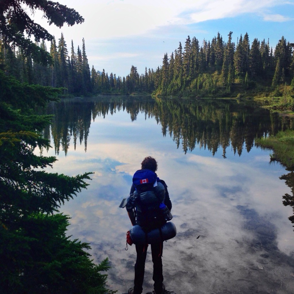 A hiker pauses to take in the glassy waters of Arnica Lake.