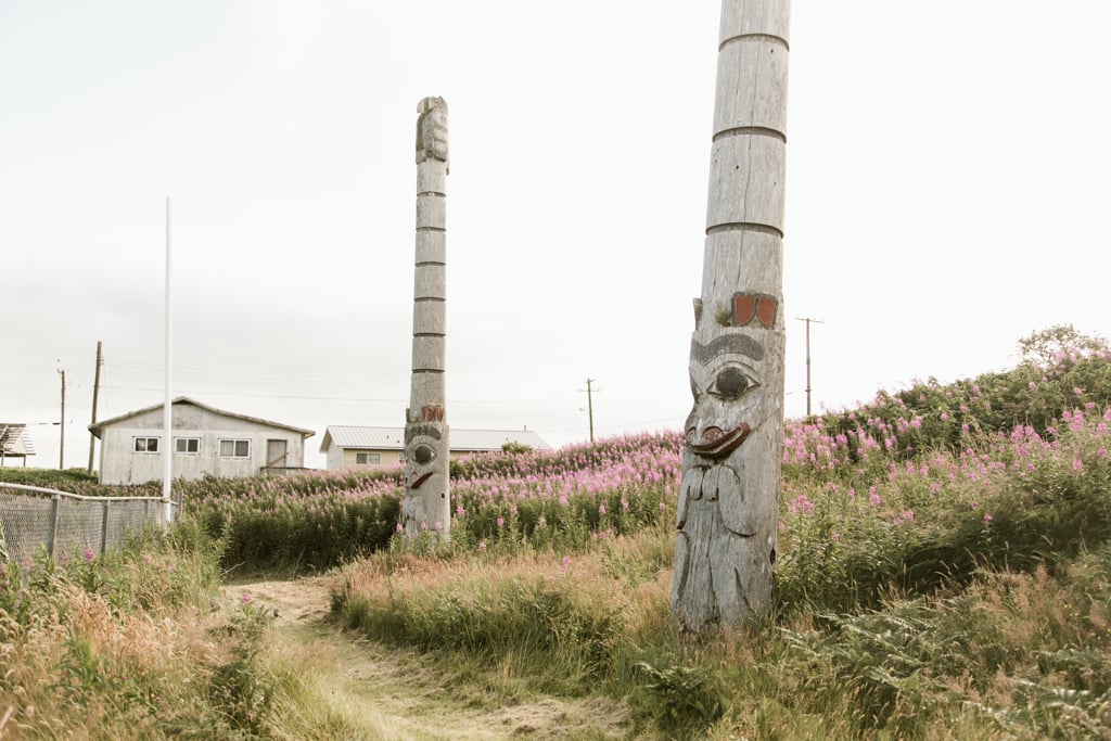 Tall poles carved from red cedar sit in a field of blooming flowers.