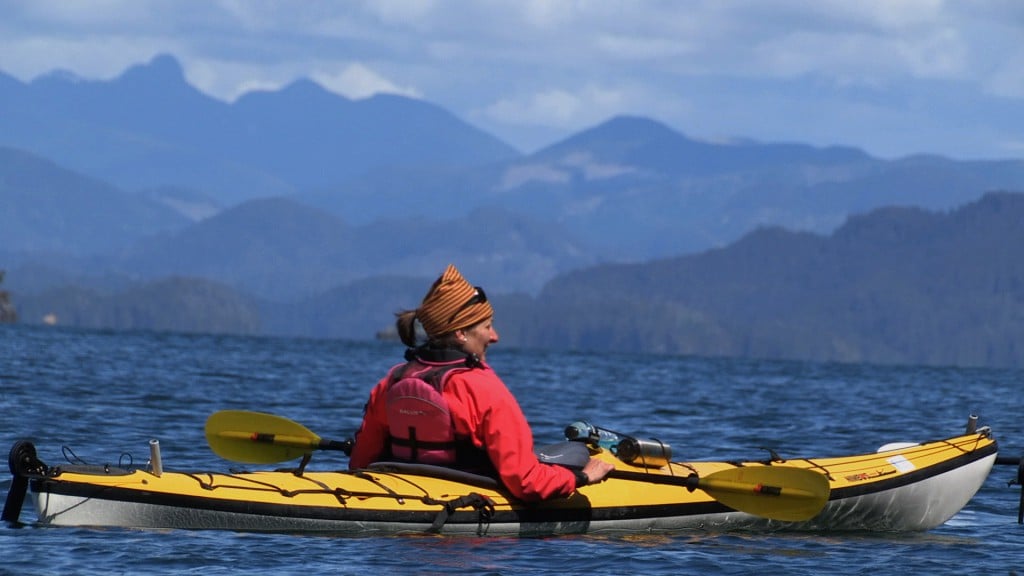 A woman paddles through the ocean in a yellow kayak.