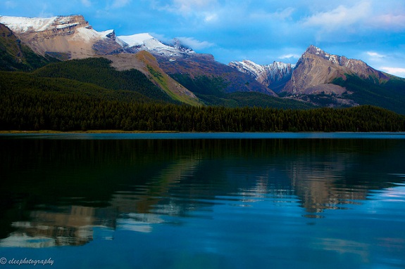 Jasper National Park's mountain peaks reflecting in a still lake with blue skies above.