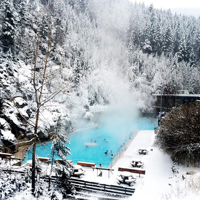 A bright blue hot spring is surrounded by a snowy landscape