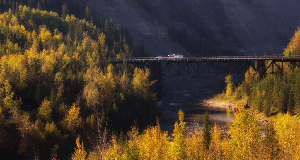 Vehicles travel across a bridge in a landscape dotted with bright fall foliage.