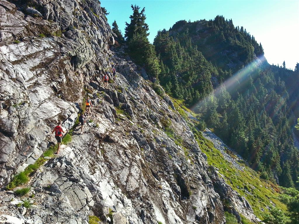 Trail runners make their way up a rocky cliff face on a sunny day.