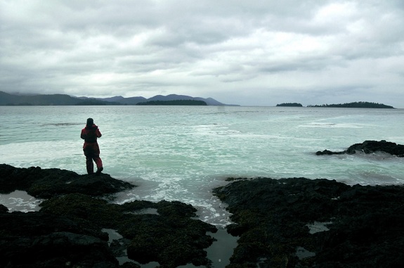 Silhouette of a woman standing at the edge of a turquoise ocean under a cloudy sky.