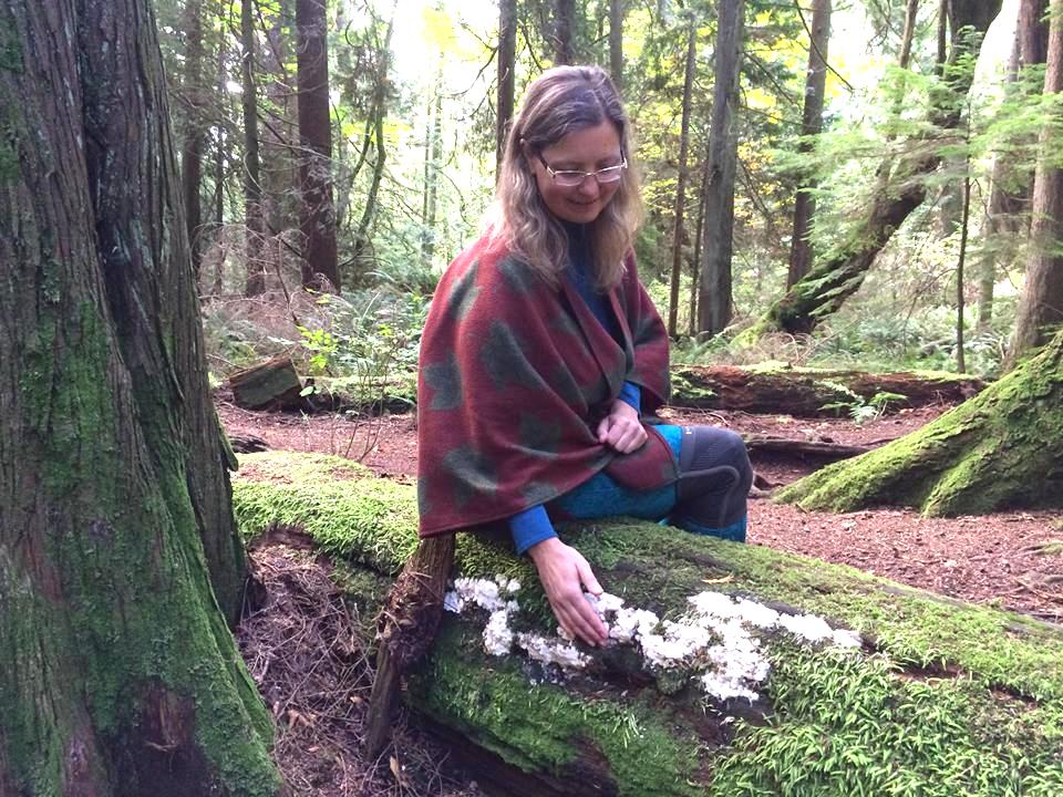 A woman sits on a moss-covered fallen log in the forest.