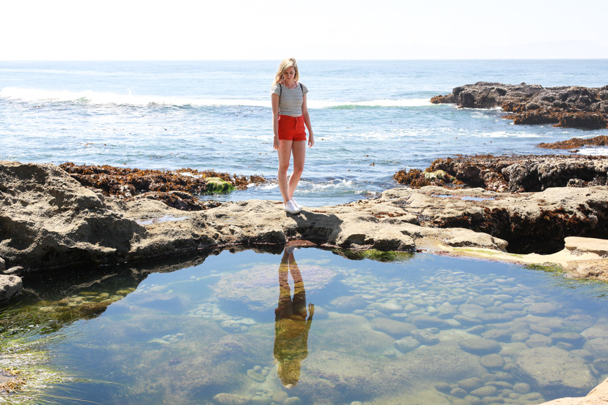 A woman stops to look at her reflection in a tidal pool.