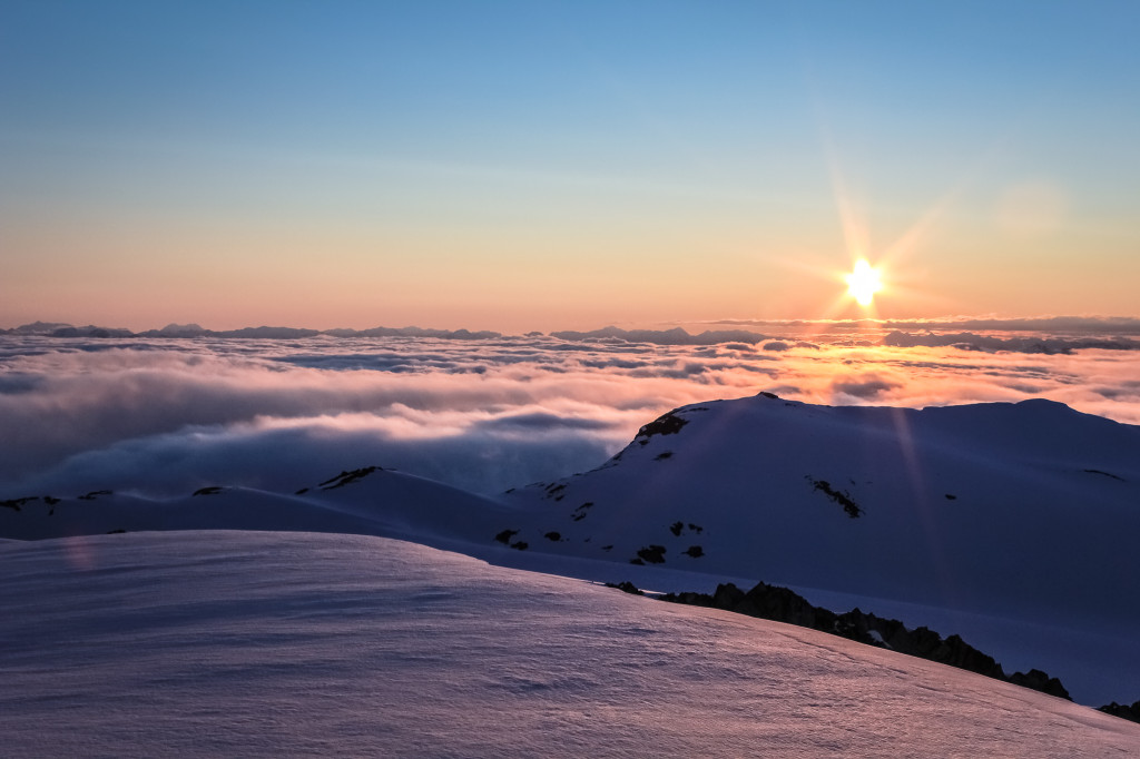 A stunning sunset over snow-covered mountains peeking above the clouds.
