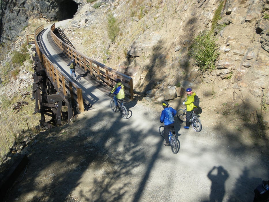 A group of cyclists traverse a bridge in a rocky landscape.