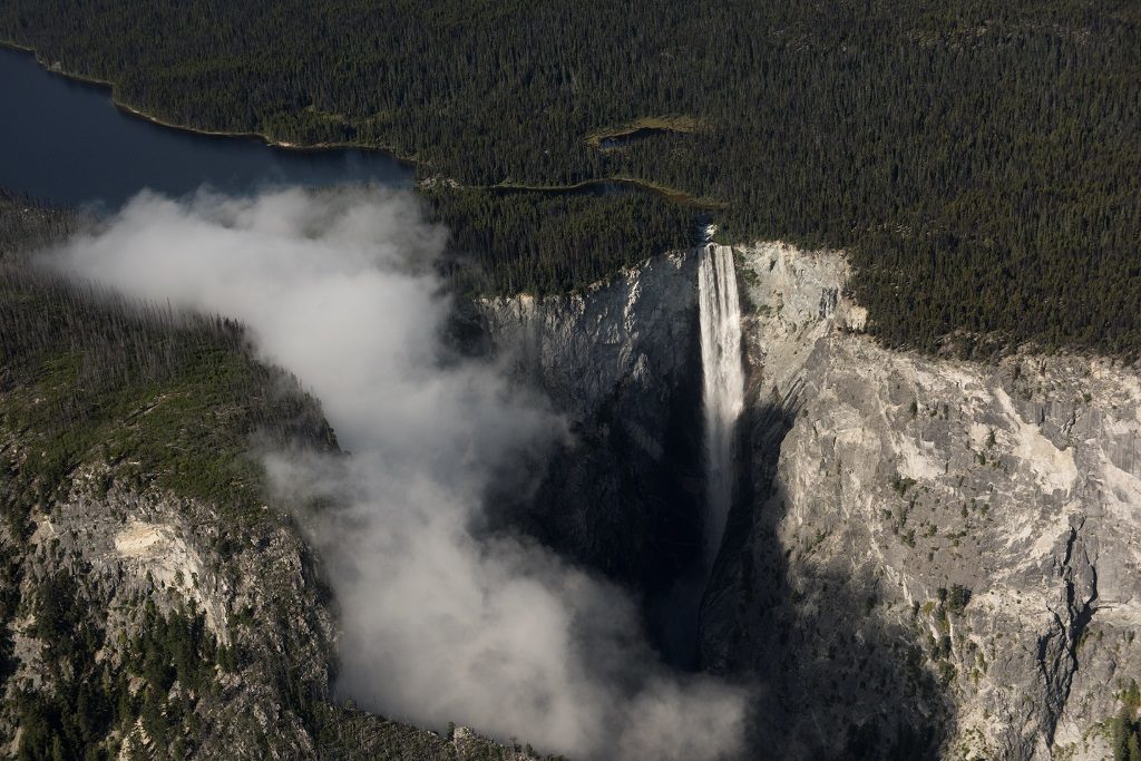Aerial view of a massive waterfall, surrounded by a dense forest.