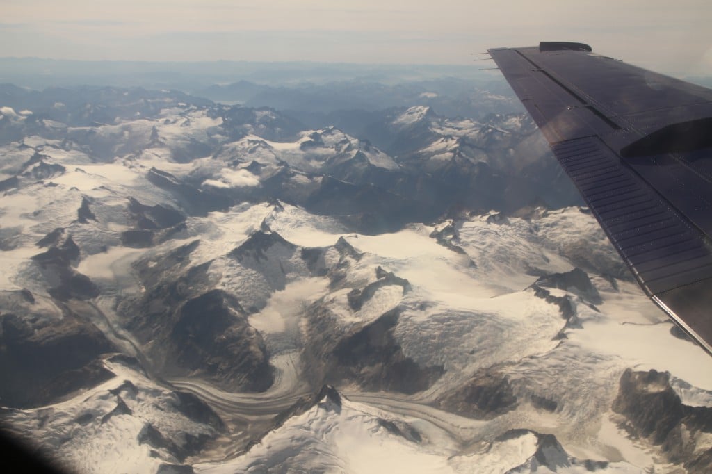 Looking out at snow-covered mountain peaks from the window of an airplane.