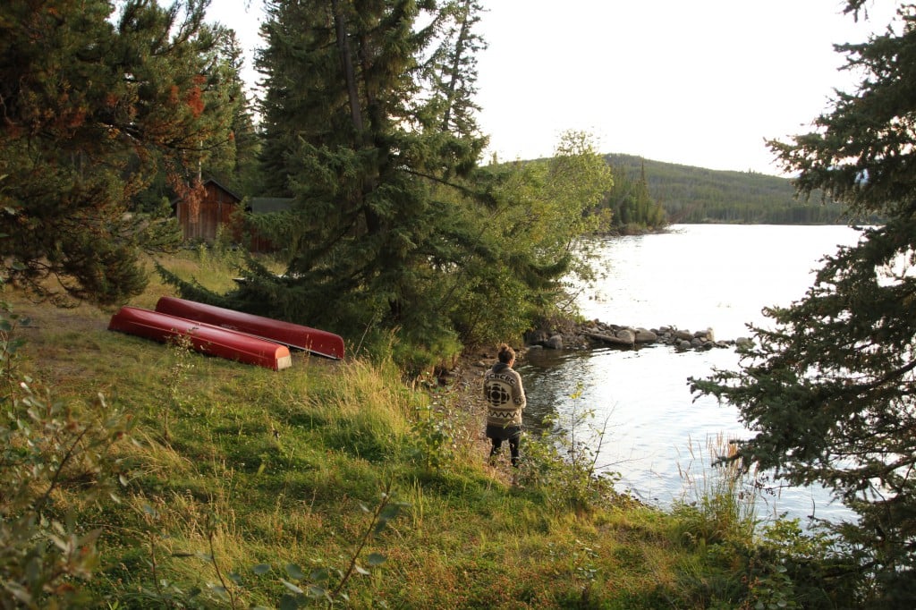 A woman and two red canoes on the edge of the water.