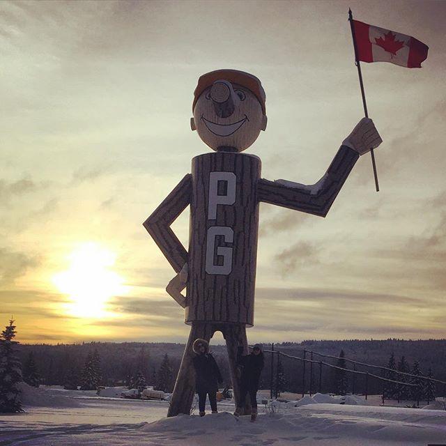 A statue depicting a giant man made of wood and holding a Canadian flag with the initials “PG” on his chest.
