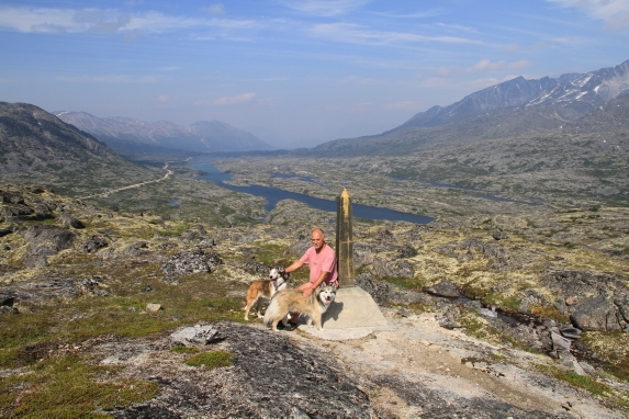 A man poses with his two dogs in the middle of a rocky landscape.