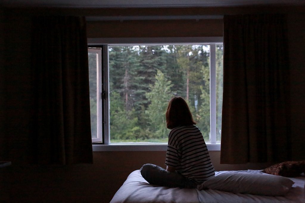 Silhouette of a woman sitting on a bed, looking out a window.