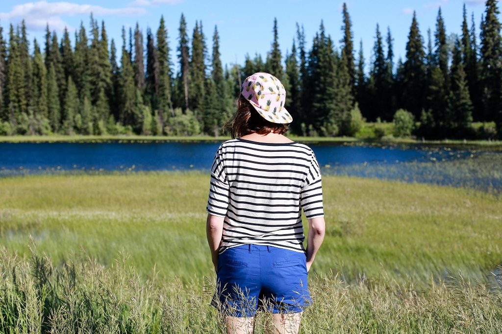 A woman in shorts and a baseball cap stands in a meadow of tall grass.