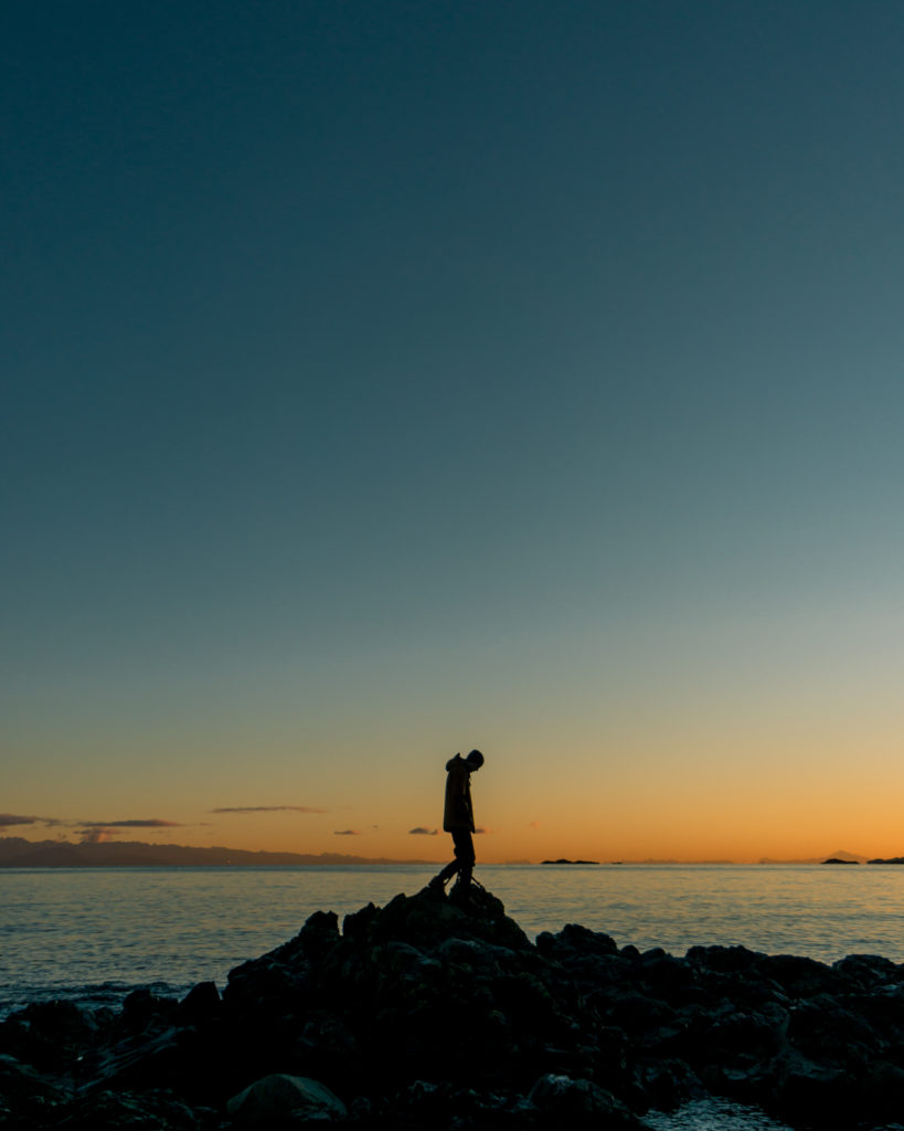 Silhouette of a man standing on a rock in front of the ocean at sunrise.