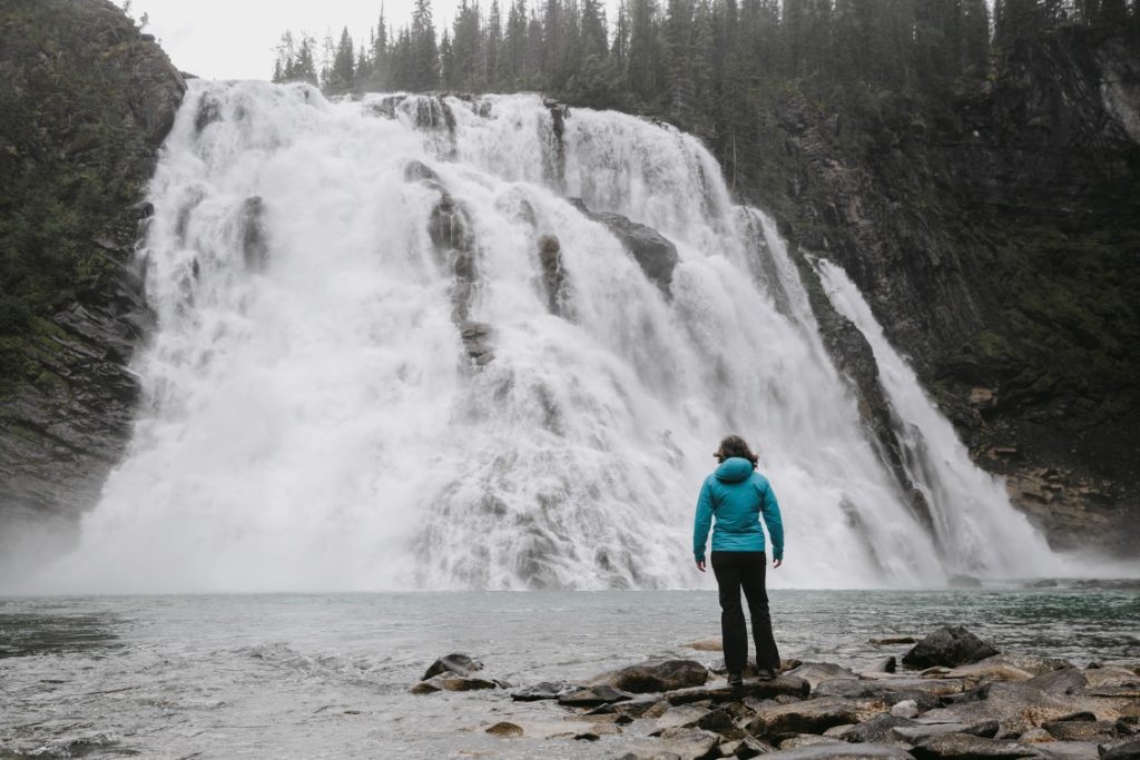 A person standing on the shore just before a large waterfall.