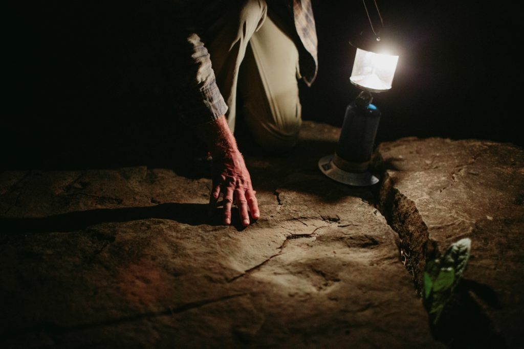 A lamp illuminates a fossilized footprint in a rock.