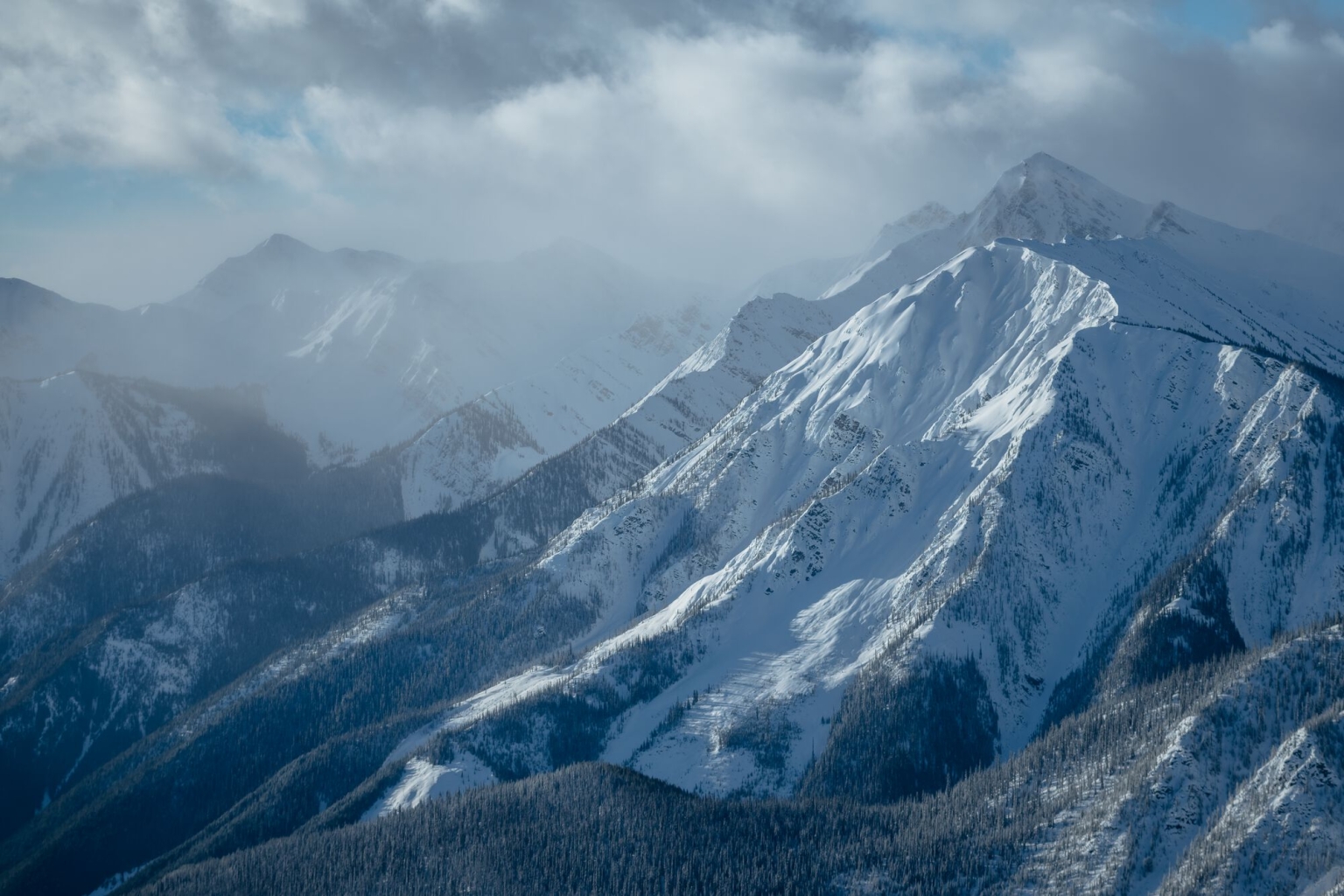 Aerial view of imposing, snow-covered mountains with a foggy sky