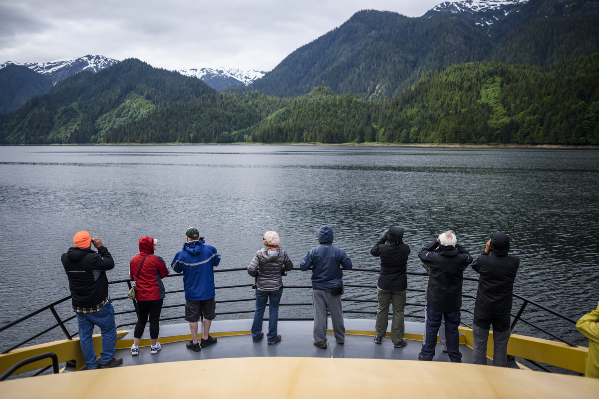 A group of adults look out on the back of a boat at the inlet