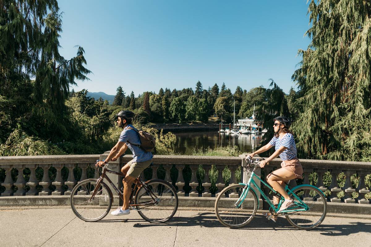 Couple cycling on bikes across a bridge in Stanley Park in a sunny day in the summer.