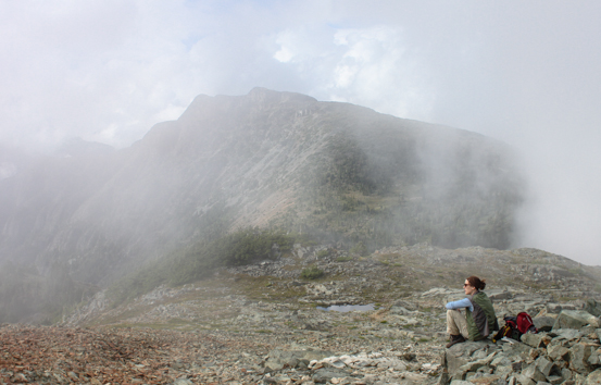 A woman sits in a rocky landscape, covered by rolling fog,