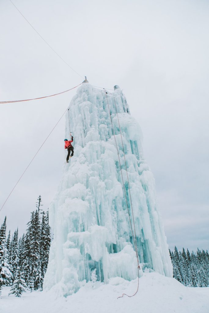 An ice climber scales a large wall of turquoise ice.