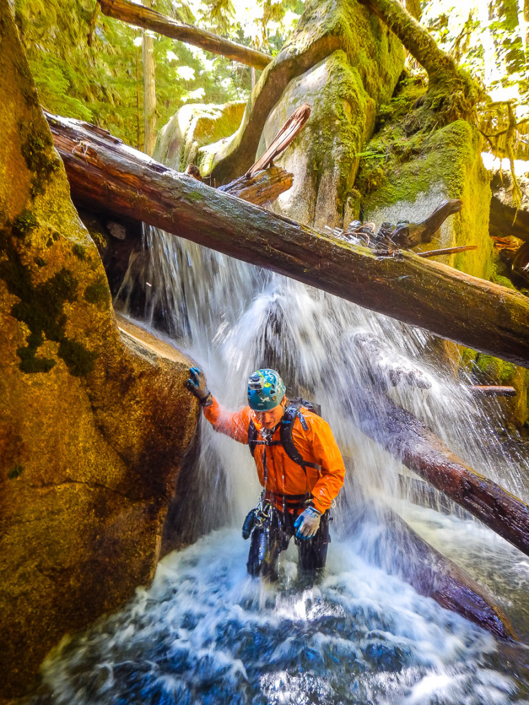 A man wearing a helmet walks under the cascading water of a waterfall.