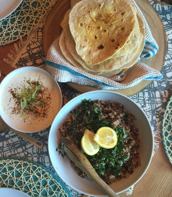 A flat lay of three beautifully prepared dishes of naan bread, wild rice, and a bowl of soup.