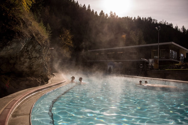 People relax in a crystal-clear hot spring pool, surrounded by trees.