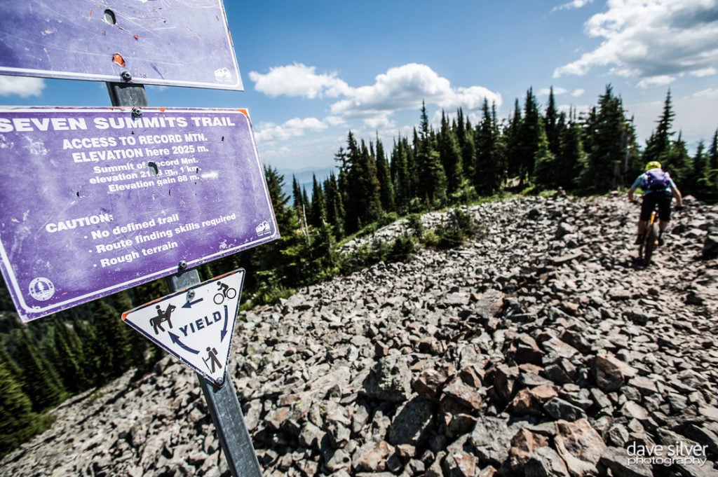 A man pedals on a rocky terrain and a sign that reads “Seven Summits Trail”.