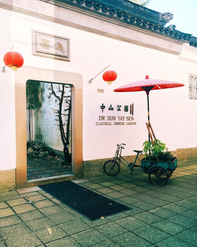 A bike with a wagon attached sits outside the stone exterior of the Yat-Sen Classical Chinese Garden.