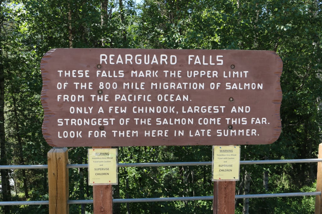 A large brown wooden sign that reads “Rearguard Falls” and describes the local salmon migration.