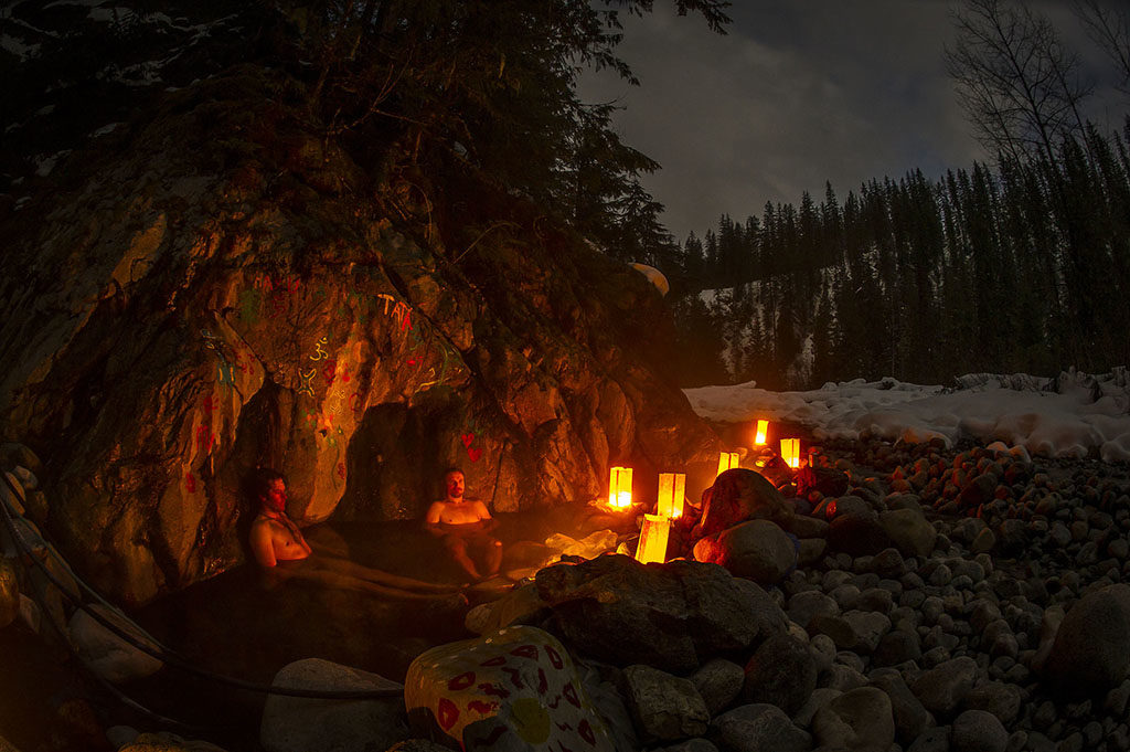 People enjoy an evening hot springs soak, lit by lanterns.